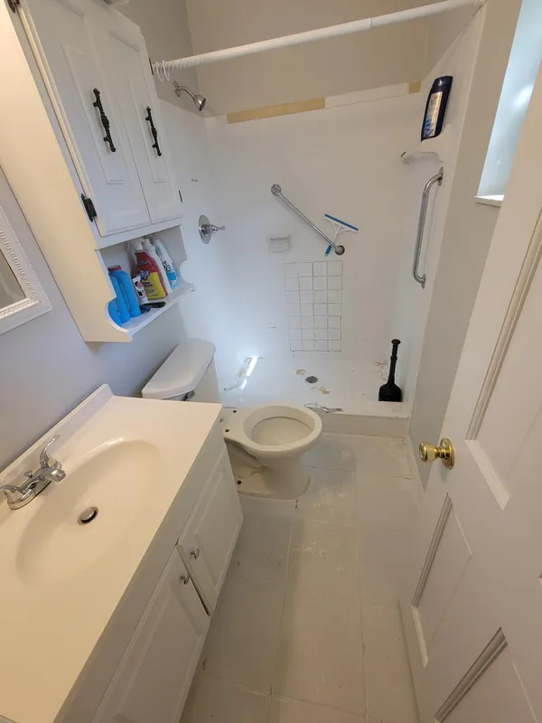 Bathroom with white vanity, toilet and a tiled tub/shower area fitted with grab bars.