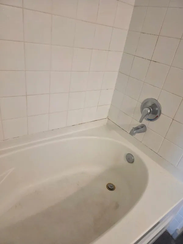 Before: white bathtub with grayish grime and residue across the tub floor and around the drain.