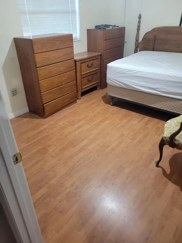 Bedroom with a neatly made bed, wooden dressers and a nightstand, and a clean laminate floor.