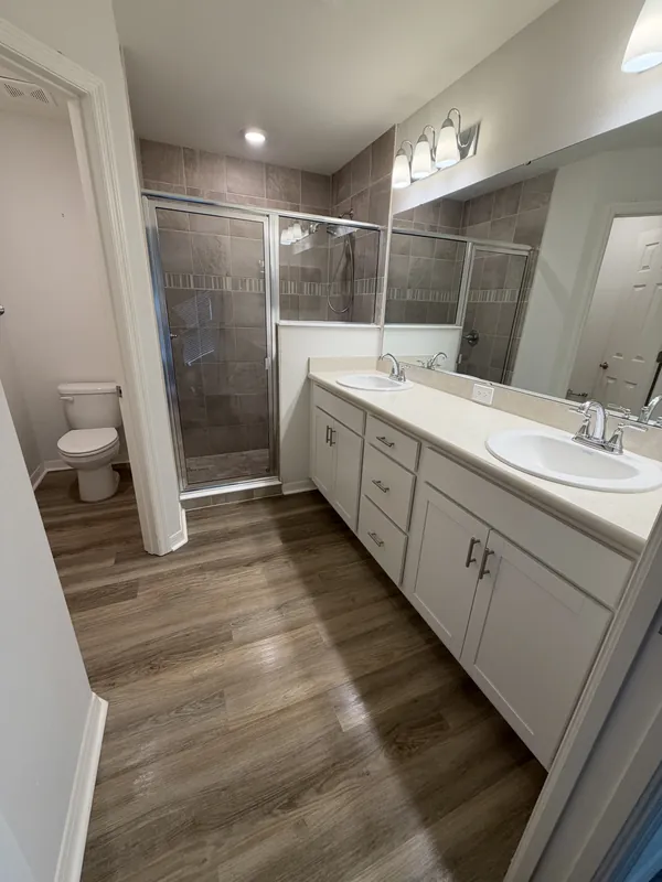 Master bathroom with a white double vanity, two sinks, glass-enclosed tiled shower and wood-look plank floor.