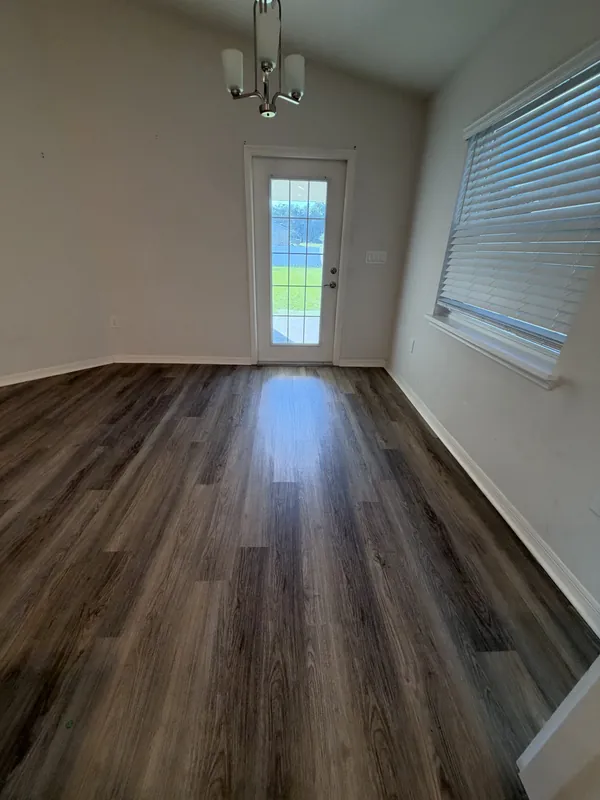 Empty dining area with a chandelier, glass back door and clean wood-look plank floor, ready for move-in.