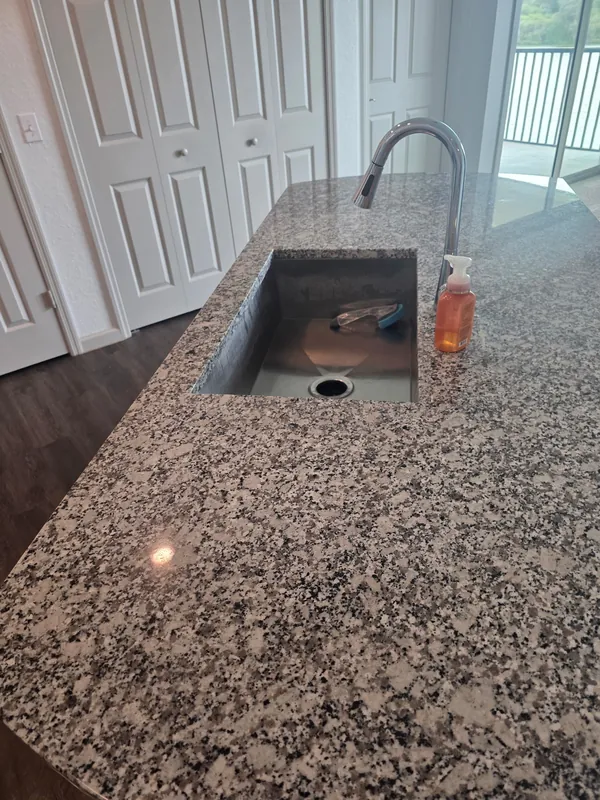 Granite kitchen island with an undermount stainless sink and arched faucet, countertop wiped clean.