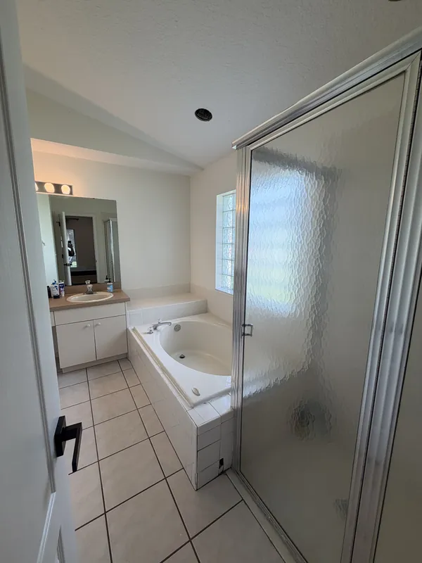 Master bathroom with a garden tub, frosted glass shower and clean white tile floor.