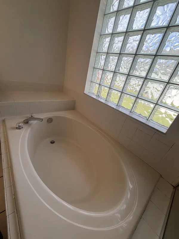Oval soaking tub under a glass-block window, clean white surfaces.
