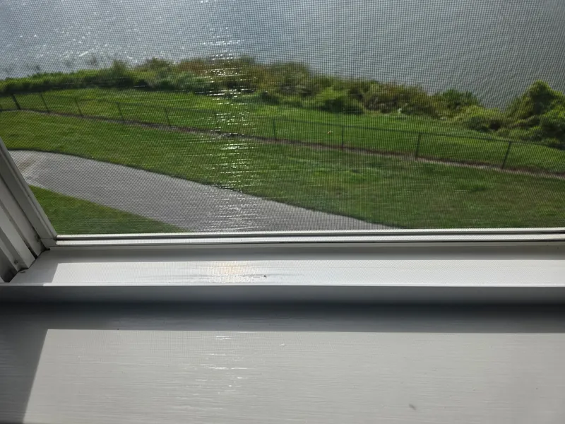 After: the same window's sill and track wiped clean, view of a grassy yard outside.